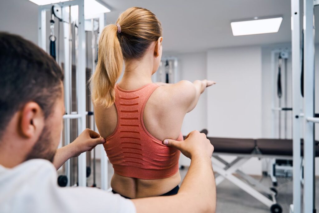 Sportmediziner Köln korrigiert Rückenhaltung bei Patientin im Trainingsraum