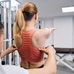 Sportmediziner Köln korrigiert Rückenhaltung bei Patientin im Trainingsraum