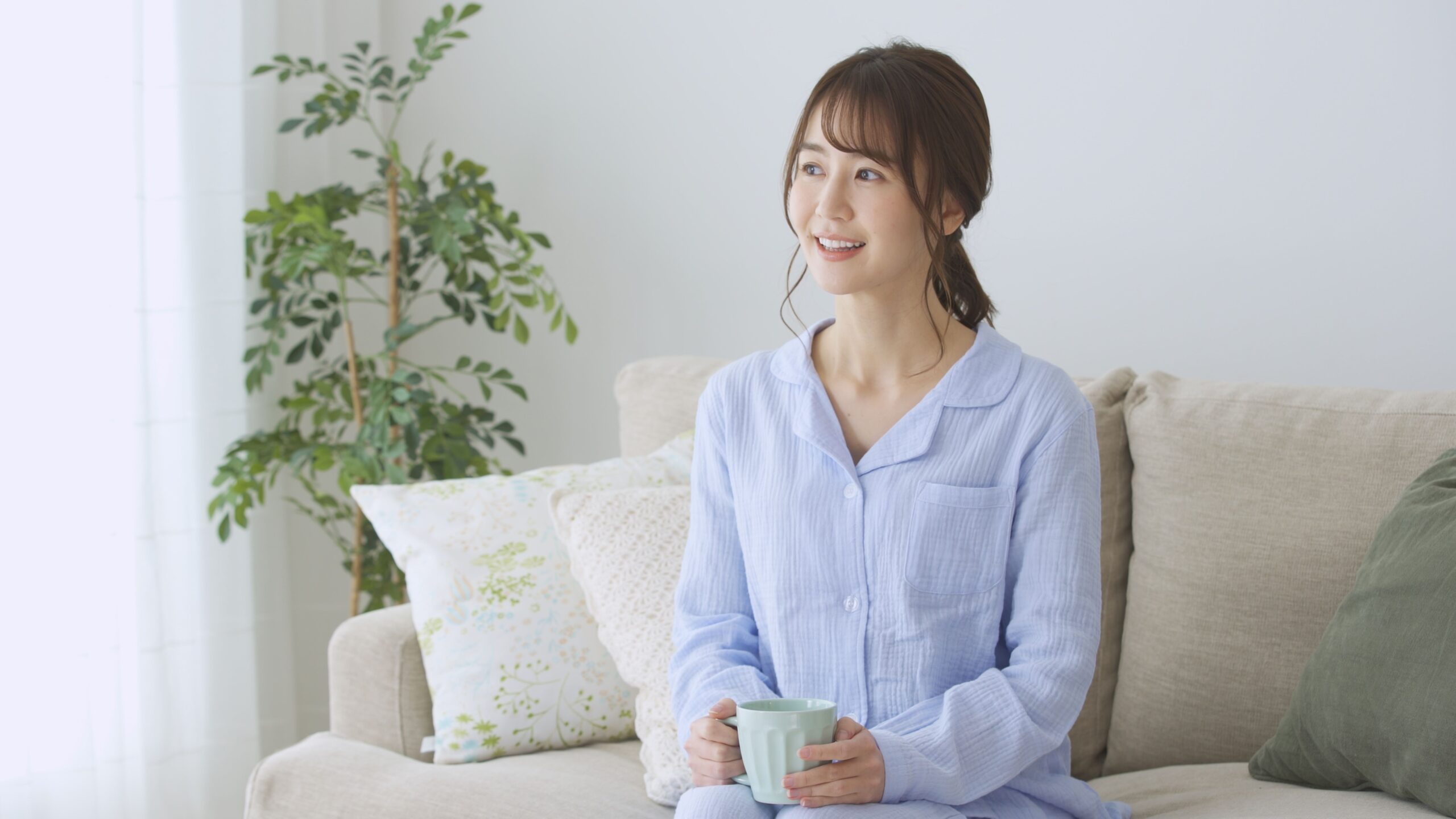 Frau sitzt entspannt auf Sofa und hält eine Tasse in der Hand – Symbol für Wohlbefinden und Gesundheit durch reines Trinkwasser