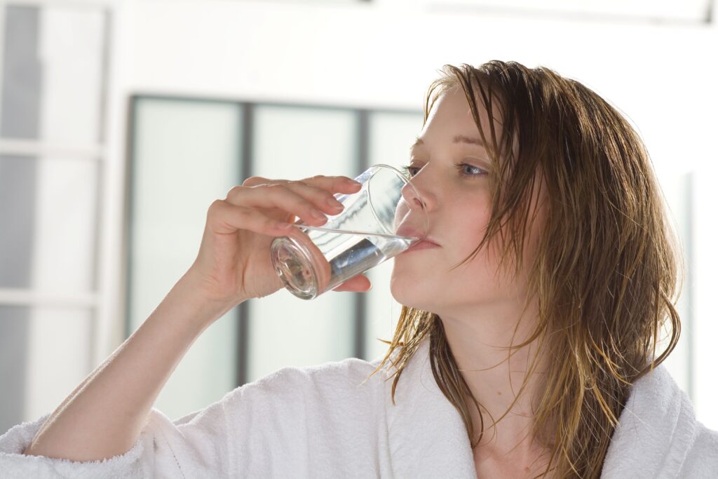 Frau trinkt klares Wasser aus einem Glas nach Nutzung einer Wasserfilteranlage für Trinkwasser